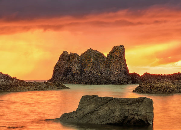Sea stack at sunset with orange sky reflected in calm Atlantic water on Irish coastline long exposure photography