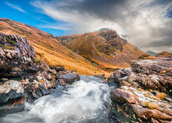 Stream flowing through a mountainous landscape in County Kerry Ireland with rocky terrain and a blue sky.