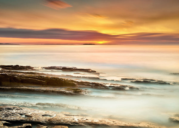 rocky Irish coastline at sunrise with golden sky and soft ocean water, long exposure minimal seascape photography Ireland