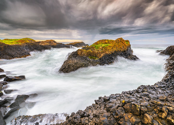 Rocks and waves on a coastal landscape with dark clouds above.
