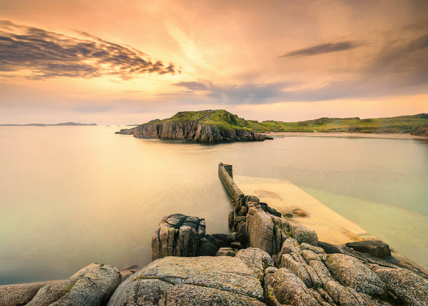Tranquil Irish coastal scene at sunset featuring rocky shores, calm waters at Boatstrand Donegal. Peaceful nature and dramatic skies. By John Taggart Landscapes