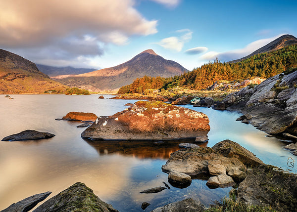 Broaghnabinne lake County Kerry Ireland with mountain peak reflections and rocky foreground during warm morning light