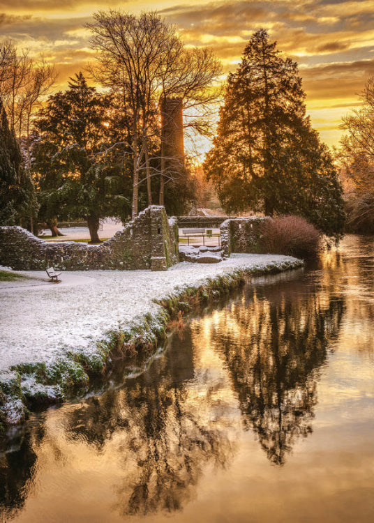 Irish castle ruins beside a river in winter with golden sunset reflections and trees