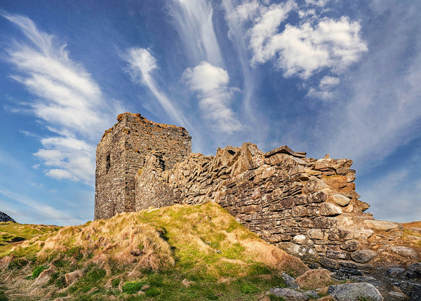 ancient stone castle ruins on grassy hill in County Cork Ireland beneath dramatic cloud filled blue sky