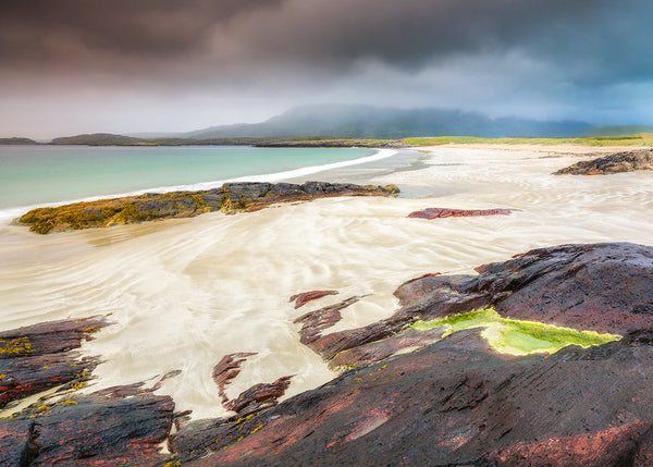 Stunning coastal landscape with rocky shore and turquoise water under a stormy sky.