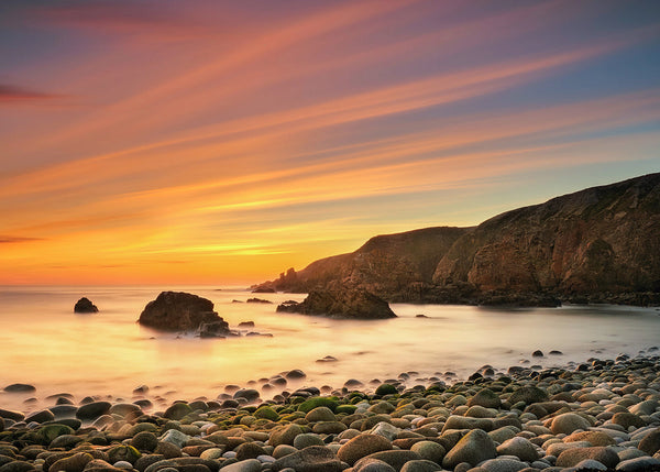 Rocky Donegal beach at sunset with smooth long exposure sea and warm pastel sky, Irish coastal landscape photography