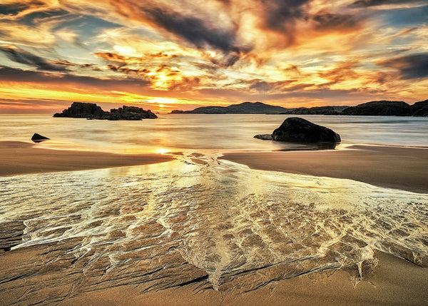 Golden sunset over Donegal beach with flowing water patterns across sand and dramatic sky reflections, Ireland landscape photography