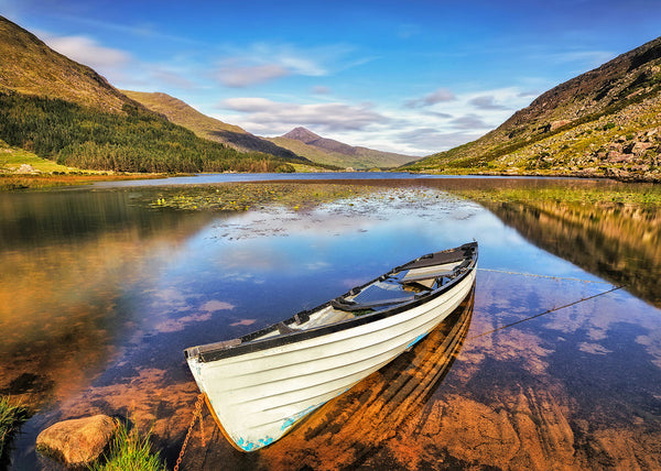 traditional white boat on a calm lake in County Kerry with mountains reflected in still water Ireland