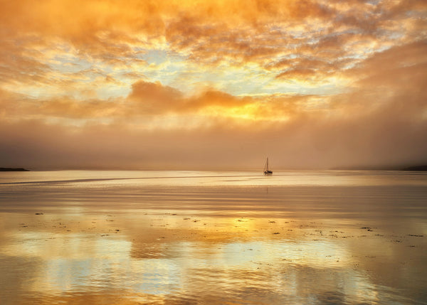 Golden sunrise over Dingle Bay Kerry Ireland with calm water reflections and lone boat silhouette