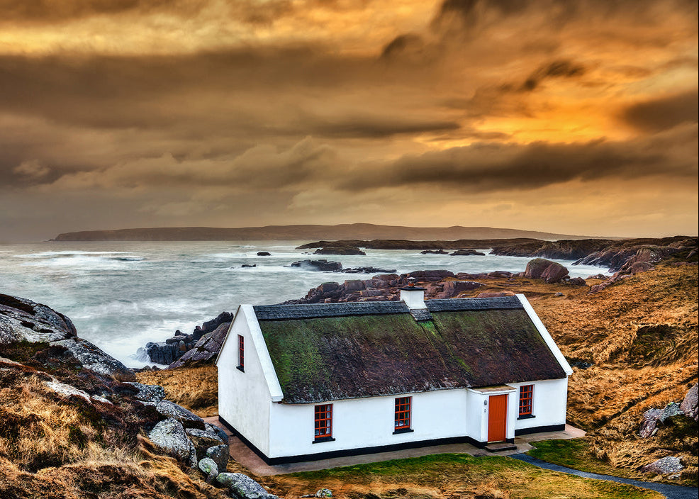 Traditional white Irish cottage with mossy roof overlooking rugged Donegal coastline at sunset, Ireland landscape photography print
