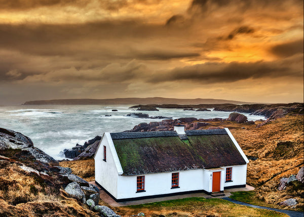Traditional white Irish cottage with mossy roof overlooking rugged Donegal coastline at sunset, Ireland landscape photography print