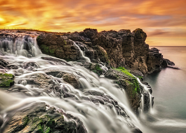 Waterfall flowing over rocky cliffs into the sea at sunset in Dunseverick, Northern Ireland coastal landscape photography