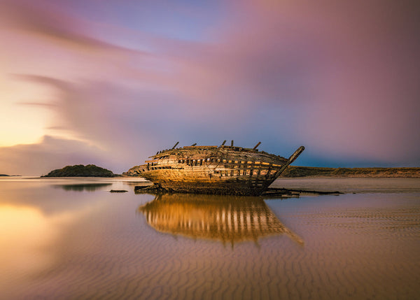 Experience the soft, cinematic beauty of the Irish coast at golden hour with this landscape photograph on Magherclogher in County Donegal. Captured as the sun melts into the Atlantic, the sky ignites with warm tones of pink, purple and gold, mirrored perfectly across the wet sand below.

This peaceful coastal scene reflects the wild, untamed character of Ireland’s west coast — a place where light, weather and land come together in fleeting, unforgettable moments. 