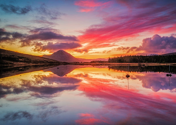 Mount Errigal reflected in calm lake at sunset Donegal Ireland with vibrant pink and orange sky landscape photography