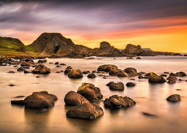 Rocky shoreline at Ballintoy Harbour County Antrim at sunset with long exposure water and warm golden sky