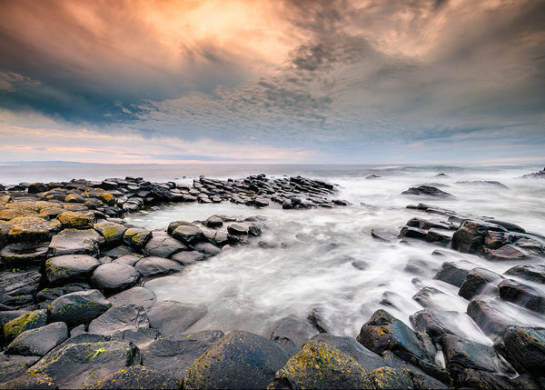Stony coastline with ocean waves and a dramatic sky. Evening light across the stones at the Giants Causeway in County Antrim