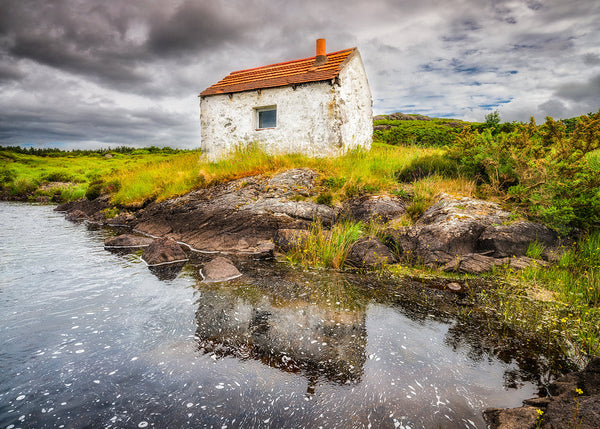 Gillies Hut Connemara cottage beside lake under dramatic Irish skies