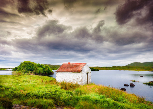 Gillies Hut Connemara cottage beside lake under dramatic Irish skies
