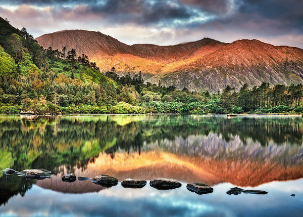 Irish mountain lake reflection with golden sunlight on hills and forest mirrored in calm water, scenic Ireland landscape photography