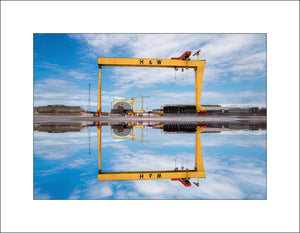 Standing tall against a vivid Belfast sky, the iconic Harland & Wolff cranes—Samson and Goliath—are perfectly mirrored in water, creating a striking symmetry. A powerful symbol of the city's shipbuilding heritage, this image captures the strength, scale, and beauty of Belfast’s industrial past and present. A moment of calm in the heart of the docks. By John Taggart Landscapes