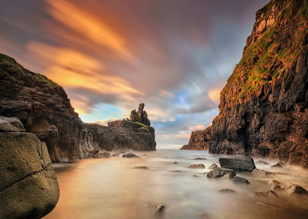 Hidden sea stack between cliffs at sunset on the Antrim Coast Ireland with long exposure silky water and glowing sky