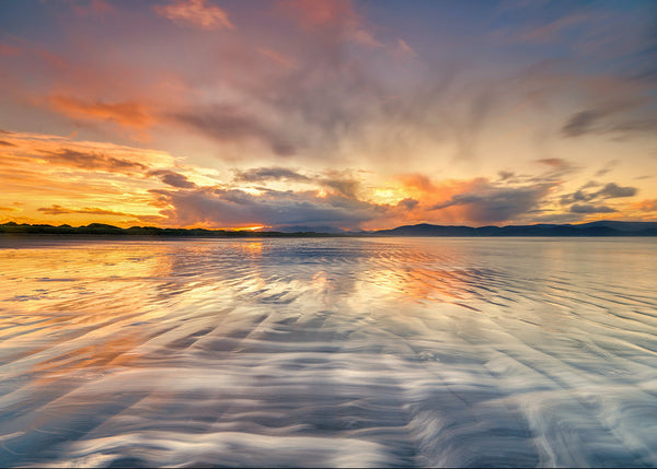 Sunset reflections on wet sand at Inch Strand County Kerry with mountains in the distance