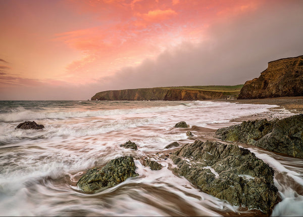 Waves flowing around rocks at Kilfarrasy Beach on the Copper Coast in County Waterford at sunset.