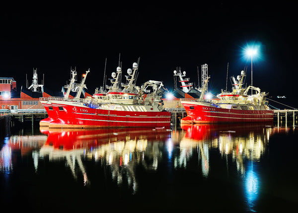 The red fishing boats lit up against a dark sky at the beautiful seaside village of Killybegs in County Donegal along the Wild Atlantic Way in Ireland.