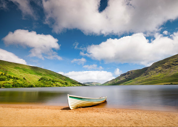 Boat on a beach with a scenic view of mountains and blue sky at Lough Na Fooey in Connemara County Galway Ireland