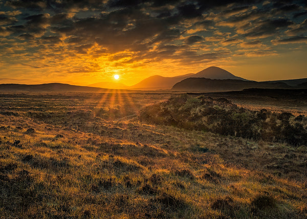 Golden sunrise over Irish mountains with dramatic clouds and glowing grassland landscape by Irish landscape photographer John Taggart