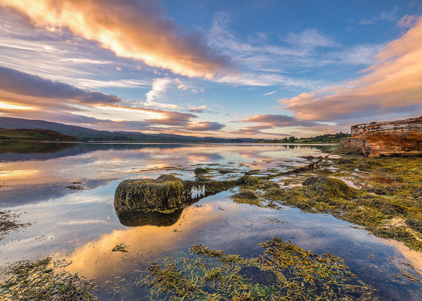 Sunset over Mulroy Bay in County Donegal with vibrant pink and gold skies reflected on wet sand along Ireland’s west coast