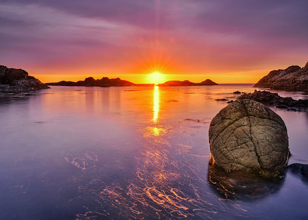 Purple sunset over calm Irish sea with glowing reflection and foreground rock long exposure photography