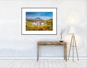 Nestled amidst the rolling hills and golden grasses of Donegal, Ireland, this weathered cottage stands as a quiet witness to generations past. With its rusted red roof and faded stone walls, it tells a story of resilience and solitude beneath the ever-watchful gaze of Mount Errigal in the distance.By John Taggart Landscapes