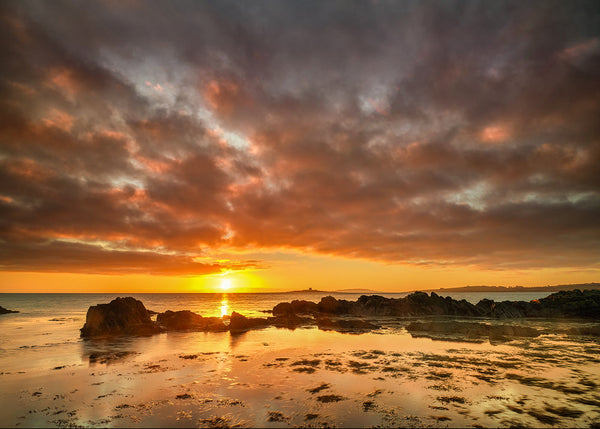 Sunrise over rocky shoreline in Skerries Dublin Ireland with golden reflections