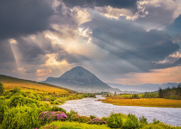 Sunbeams breaking through storm clouds over Mount Errigal and a winding river in Donegal, Ireland, captured by John Taggart Landscapes.