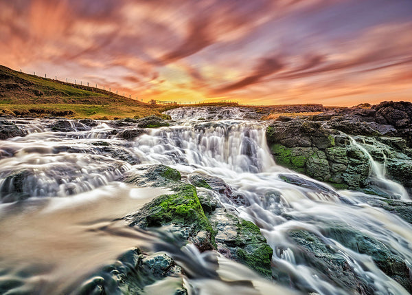 Dunseverick Falls sunset in County Antrim with flowing water over rocks and colourful sky
