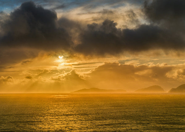 Sunset over the Blanket Islands in County Kerry ireland with large clouds and sun rays through the clouds.