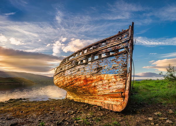 Rustic wooden boat on a grassy shore with a scenic background,The old boat The Mary Buchan at sunset in Mulroy Bay in County Donegal Ireland