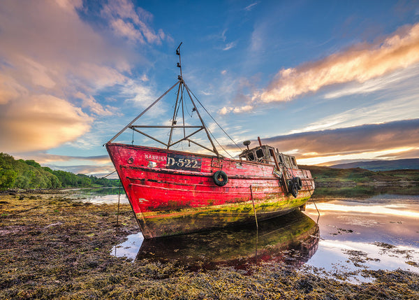 Abandoned red boat on a beach with a colorful sky