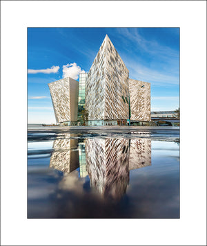 Striking architectural photography of Titanic Belfast, captured with perfect reflection and crisp detail under a blue sky. This iconic image from Northern Ireland showcases the modern design and cultural significance of Belfast's Titanic Quarter. A fine art print by John Taggart Landscapes, ideal for home or office decor.