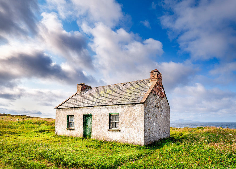 Small stone cottage on a grassy hill with a cloudy blue sky on Tory Island County Galway ireland