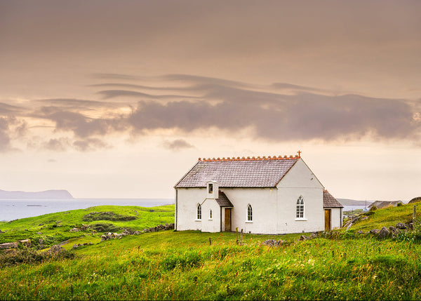 Donegal coastal church at sunset overlooking Atlantic Ocean Ireland by Irish landscape photographer John Taggart with green hills and soft evening light