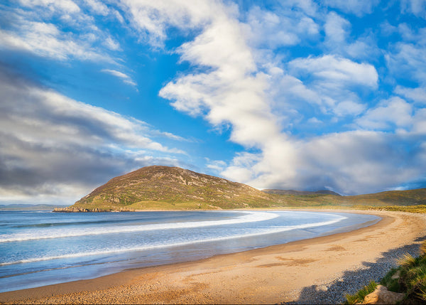 Beach with a mountain in the background under a blue sky with iclouds in County Donegal Ireland