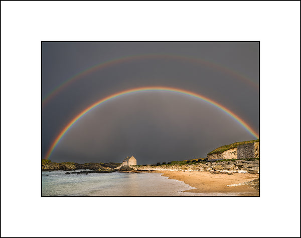 A double rainbow fills a dark moody sky at Ballintoy Harbour Co Antrim on Ireland's north coast. By John Taggart Landscape Photography